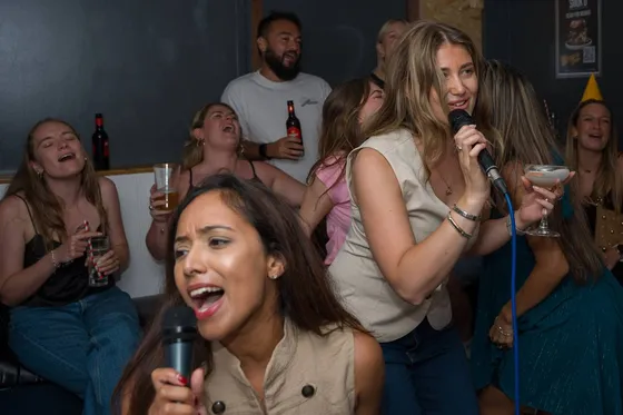 A packed karaoke room at The Old School Yard, arms in the air mid-song